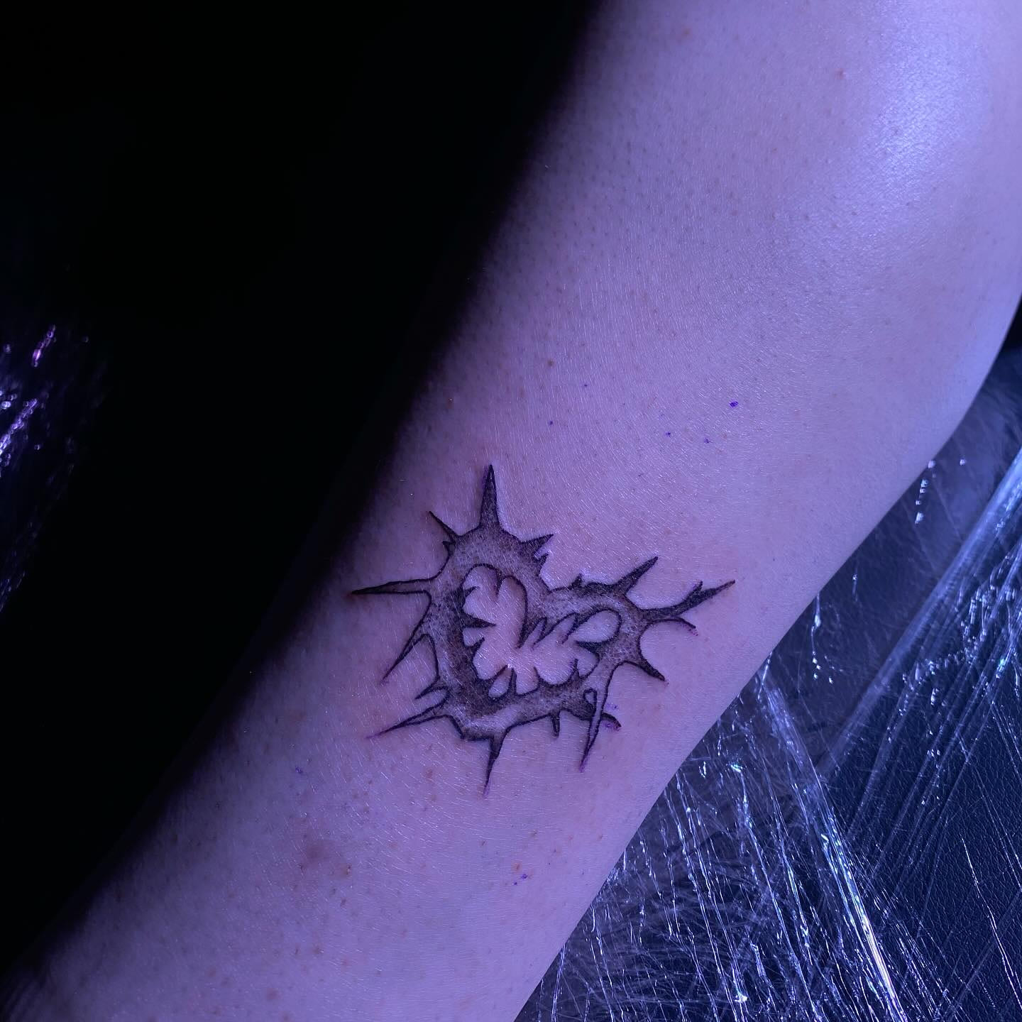 Spiked heart sigil on the forearm under cling film, violet light