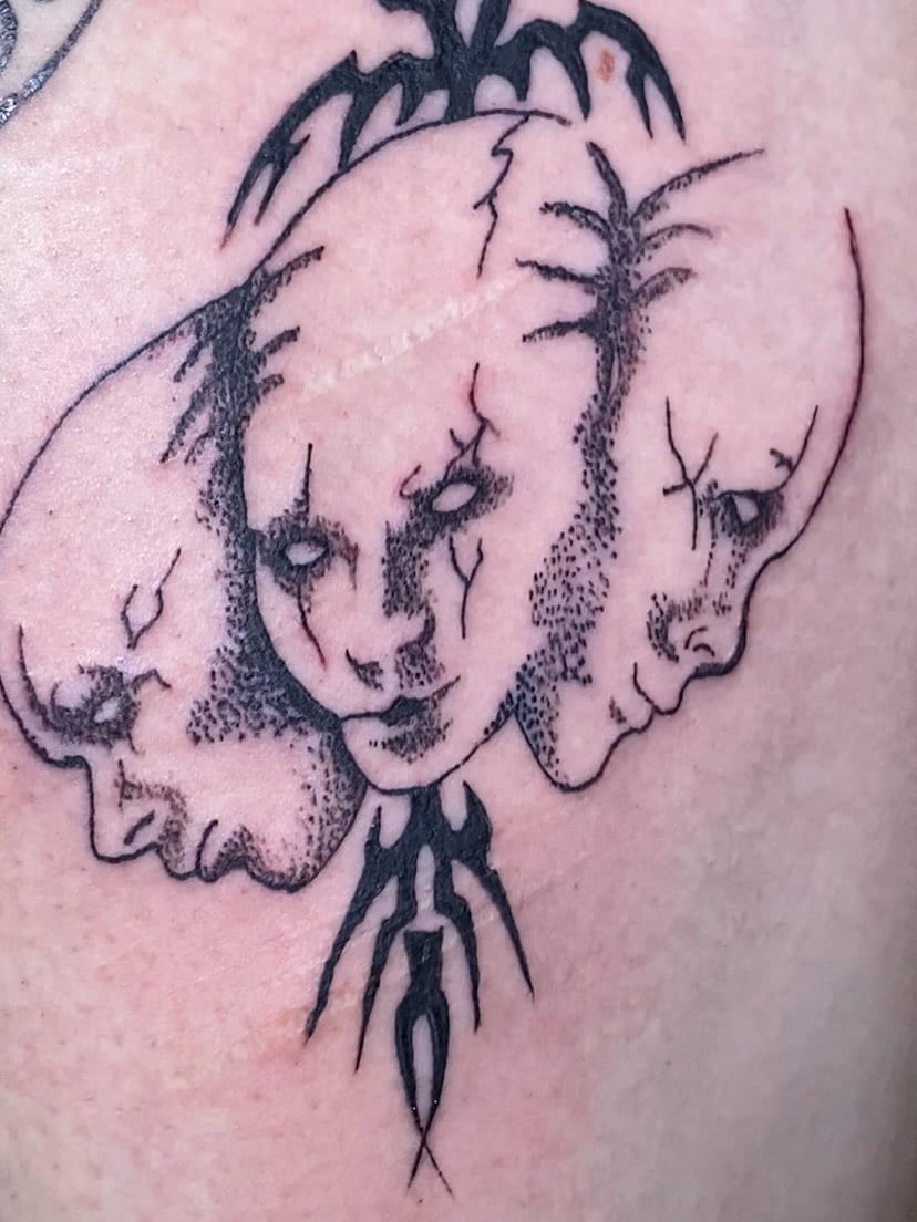 Three dotwork faces framed by tribal barbs on the thigh, fresh
